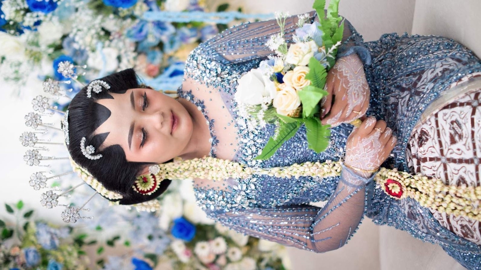 Foto pengantin adat Jawa dengan kebaya biru elegan dan riasan paes lengkap.